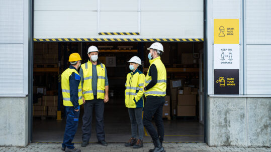 Group of workers with face mask talking in front of warehouse, coronavirus concept.