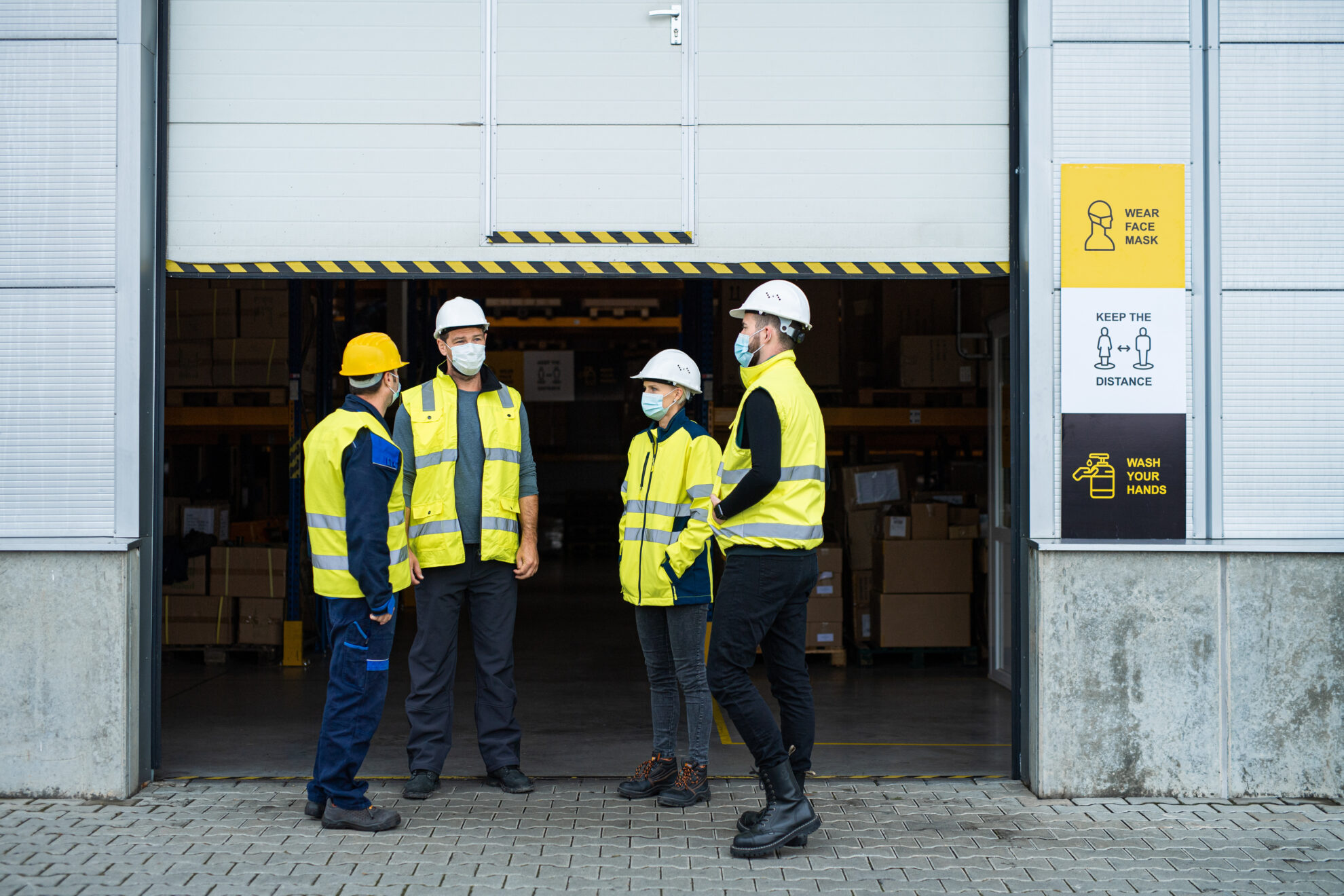 Group of workers with face mask talking in front of warehouse, coronavirus concept.